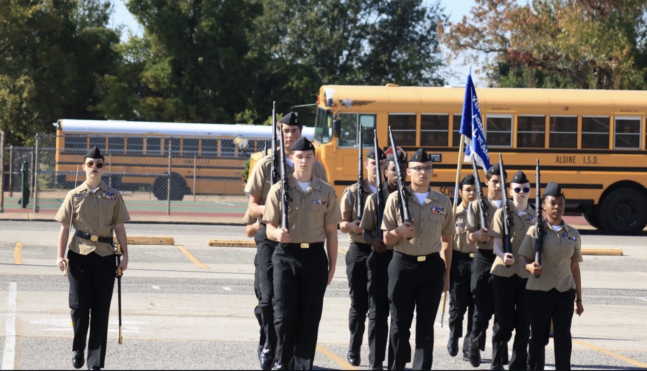 Kingwood NJROTC armed drill team marching in tan and black uniforms carrying drill rifles